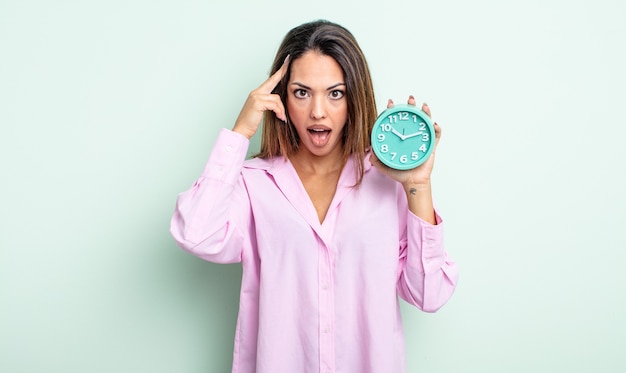 Pretty hispanic woman looking surprised, realizing a new thought, idea or concept. alarm clock concept