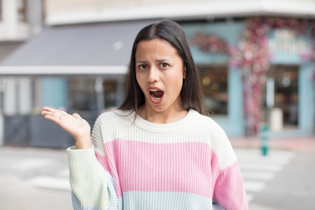 驚いてショックを受けたかなりのヒスパニック系の女性が、横に開いた手でオブジェクトを持って顎を落とした