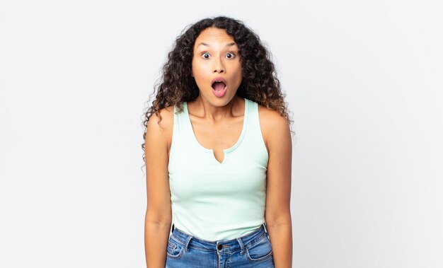 Pretty hispanic woman looking very shocked or surprised, staring with open mouth saying wow