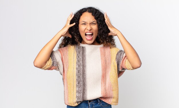 Pretty hispanic woman screaming with hands up in the air, feeling furious, frustrated, stressed and upset