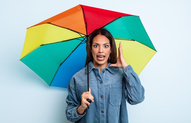 Pretty hispanic woman screaming with hands up in the air. umbrella concept