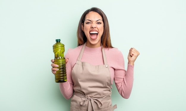 Pretty hispanic woman shouting aggressively with an angry expression. olive oil concept