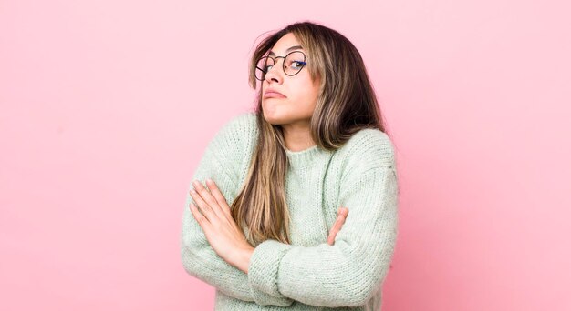 Pretty hispanic woman shrugging feeling confused and uncertain doubting with arms crossed and puzzled look