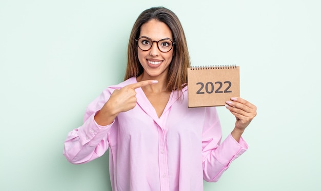 Pretty hispanic woman smiling cheerfully feeling happy and pointing to the side 2022 calendar concept