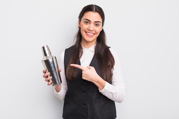 Pretty hispanic woman smiling cheerfully feeling happy and pointing to the side barman cocktail concept