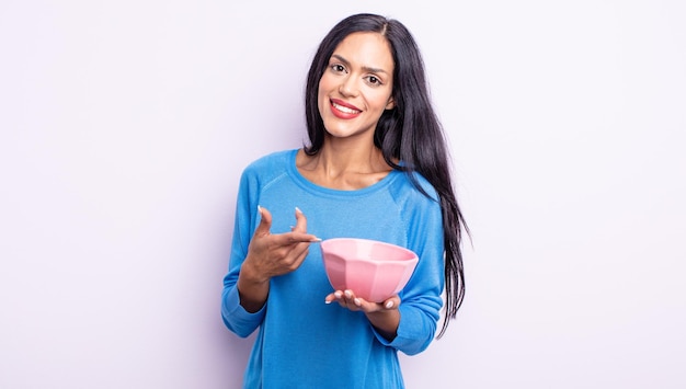 Pretty hispanic woman smiling cheerfully, feeling happy and pointing to the side. empty bowl concept