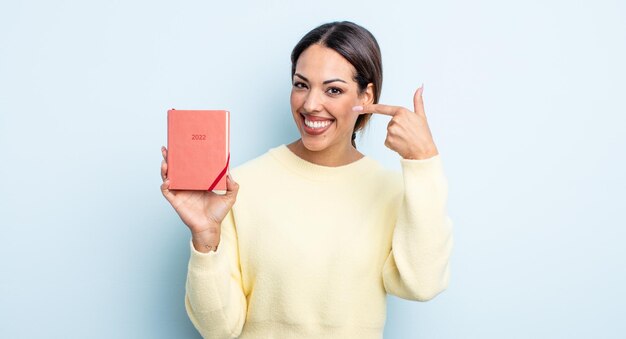 Pretty hispanic woman smiling confidently pointing to own broad smile. agenda concept