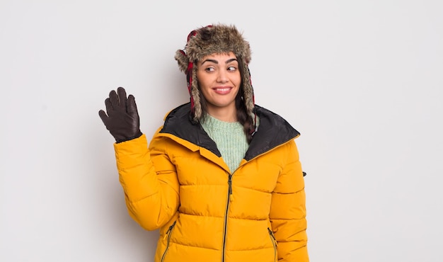 Pretty hispanic woman smiling happily, waving hand, welcoming and greeting you. cold weather concept