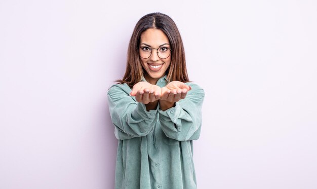 Pretty hispanic woman smiling happily with friendly, confident, positive look, offering and showing an object or concept