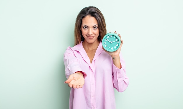 Photo pretty hispanic woman smiling happily with friendly and  offering and showing a concept. alarm clock concept