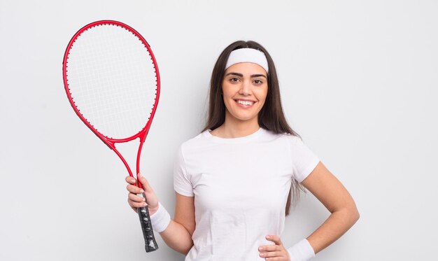 Pretty hispanic woman smiling happily with a hand on hip and confident tennis concept