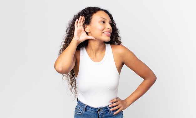 Pretty hispanic woman smiling, looking curiously to the side, trying to listen to gossip or overhearing a secret