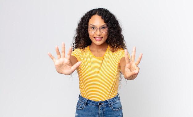 Pretty hispanic woman smiling and looking friendly, showing number eight or eighth with hand forward, counting down