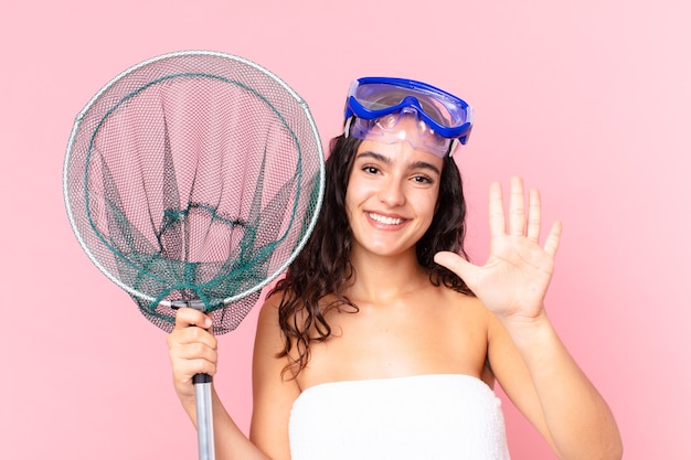 Photo pretty hispanic woman smiling and looking friendly, showing number five with goggles and fishing net