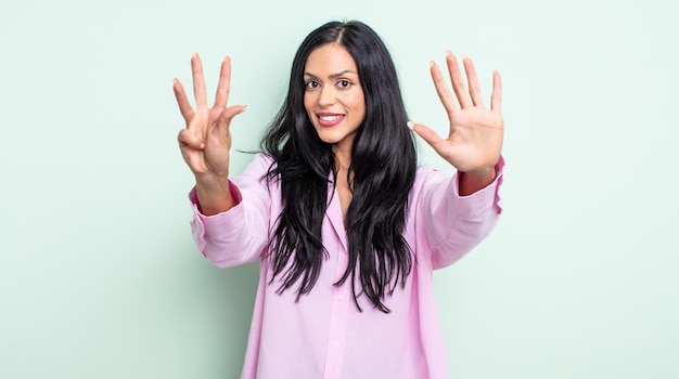 Pretty hispanic woman smiling and looking friendly, showing number nine or ninth with hand forward, counting down