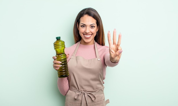 Pretty hispanic woman smiling and looking friendly, showing number three. olive oil concept