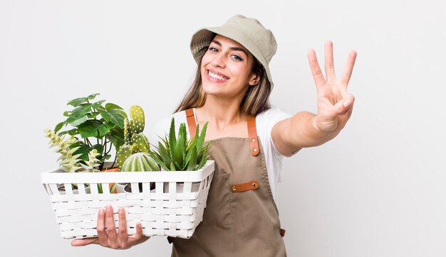 Foto bella donna ispanica sorridente e dall'aspetto amichevole che mostra il numero tre piante e il concetto di giardinaggio