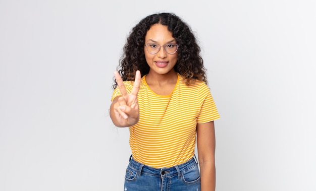 Foto bella donna ispanica che sorride e sembra amichevole, mostrando il numero due o il secondo con la mano in avanti, conto alla rovescia