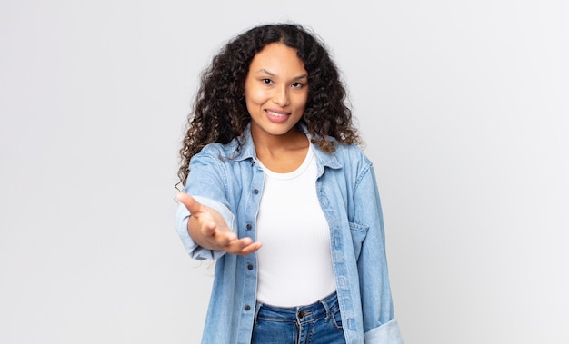 Pretty hispanic woman smiling, looking happy, confident and friendly, offering a handshake to close a deal, cooperating