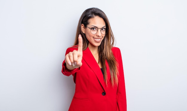 Pretty hispanic woman smiling proudly and confidently making number one. businesswoman concept