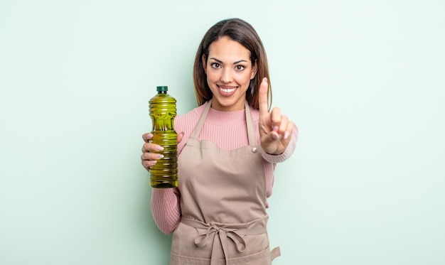 Pretty hispanic woman smiling proudly and confidently making number one. olive oil concept