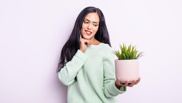 Pretty hispanic woman smiling with a happy, confident expression with hand on chin. house plant concept