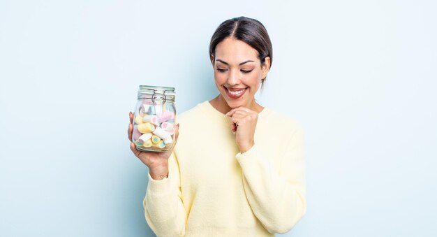 Pretty hispanic woman smiling with a happy, confident expression with hand on chin. jelly candies concept