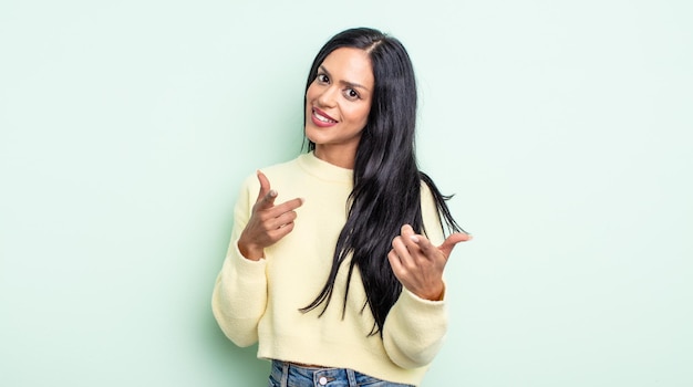 Pretty hispanic woman smiling with a positive, successful, happy attitude pointing to the camera, making gun sign with hands