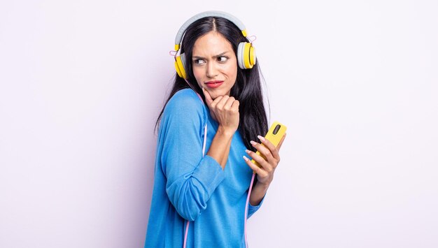 Pretty hispanic woman thinking feeling doubtful and confused smartphone and headphones concept