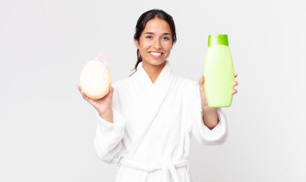 Pretty hispanic woman wearing bathrobe and holding a shampoo and a sponge