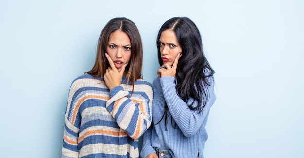 Pretty hispanic woman with mouth and eyes wide open and hand on chin. couple of friends concept