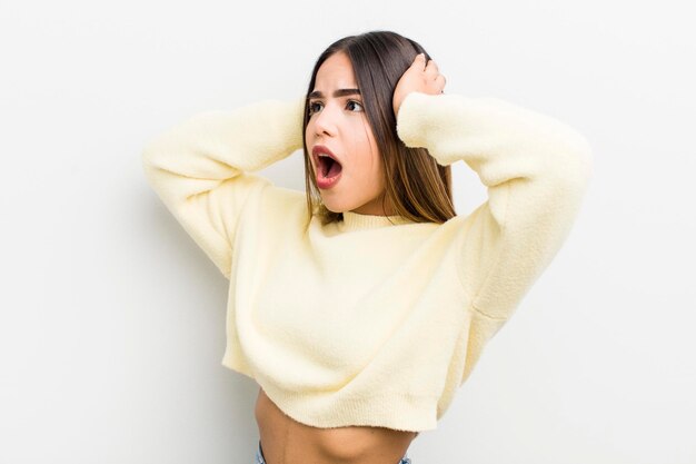 Pretty hispanic woman with open mouth looking horrified and shocked because of a terrible mistake raising hands to head