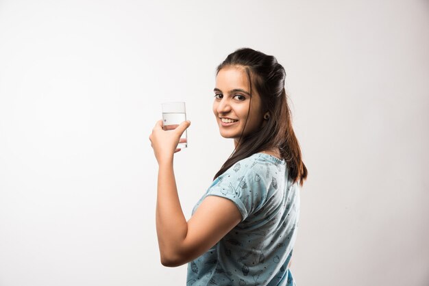 Pretty Indian Asian girl holding glass of plain water, standing isolated over white background