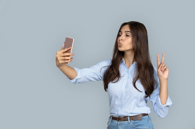 Pretty indian blogger making selfie kiss face victory sign portrait