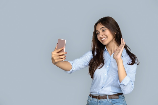 Pretty indian girl making selfie waving hand look at cellphone