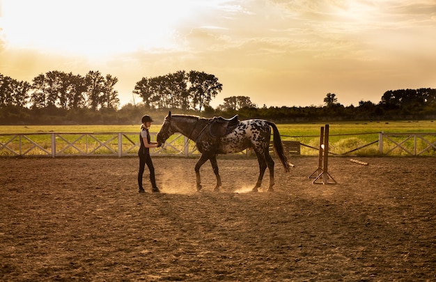 Pretty jockey girl is standing near a horse kissing and hugging her