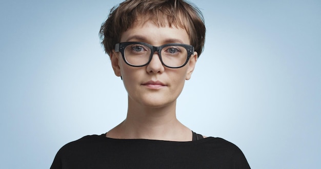 Pretty joyful smiling young woman with dark short hair wearing a black top and glasses isolated on color backgrounds