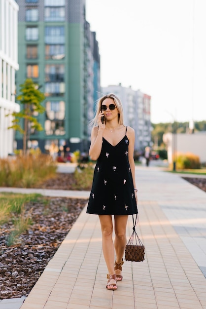 Pretty joyful woman is talking on a mobile phone while walking around the city in the summer