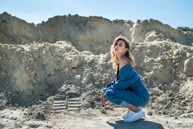 Pretty lady in blue overalls walks in a sand quarry, active way