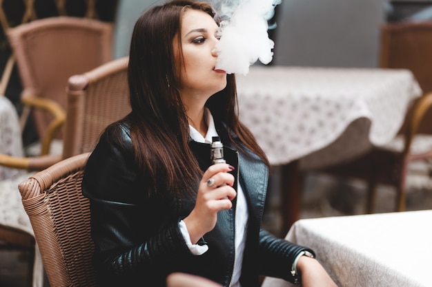 Pretty lady holding an electronic cigarette in her hand while sitting at a cafe table