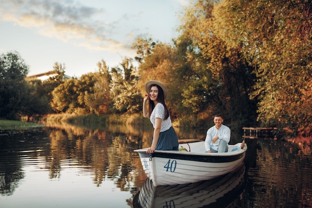 Pretty lady poses in boat on quiet lake at summer day. Romantic date, boating trip, man and woman walking along the river