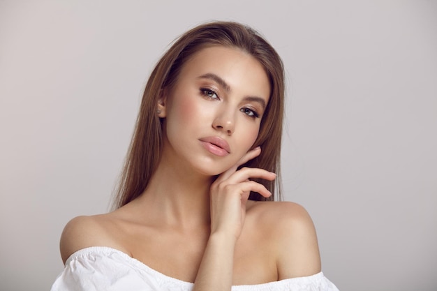 Pretty lady in white dress touches neck in light studio