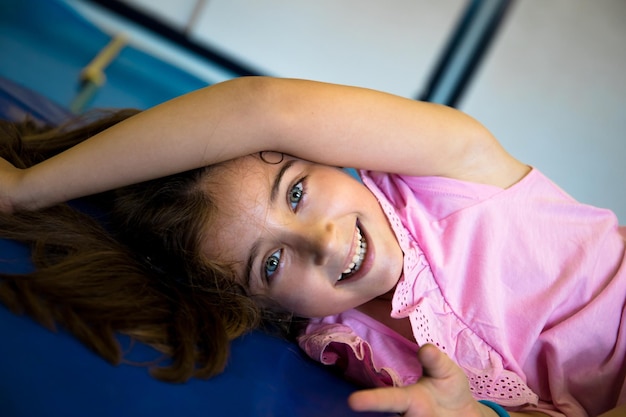 Фото Симпатичная светлоглазая девочка лежит на ковриках в школьном спортзале.