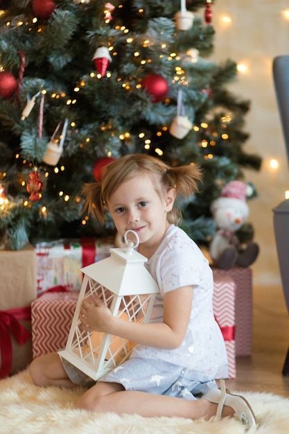 Pretty little 4 year old girl  is sitting in front of Christmas tree among presents.