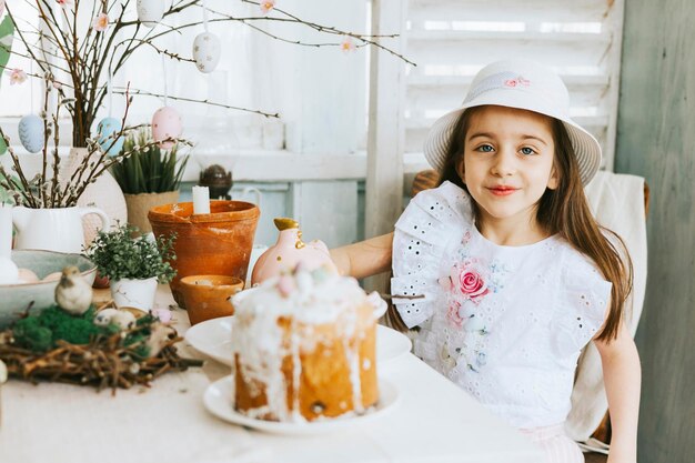 Pretty little Armenian girl helps with baking for Easter on veranda on sunny spring day decorated with flowers and Easter decor eggs cake and willow branches Easter family celebration