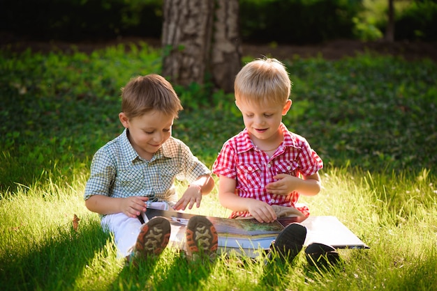 A pretty little boys reading a book on a green grass.