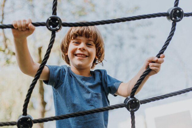 Pretty little brunette boy in a blue T-shirt is climbing a rope web. child is engaged in outdoor sports. healthy active kid. lifestyle. space for text. High quality photo