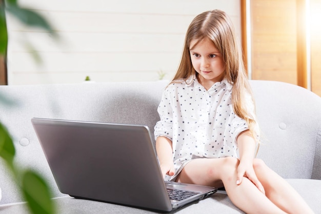 Pretty little brunette girl sitting on the sofa and using laptop