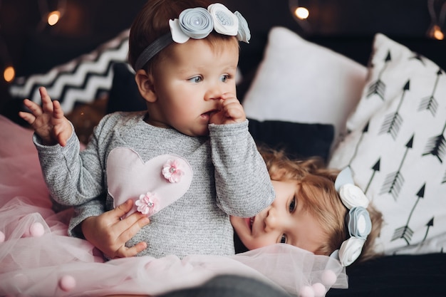 Pretty little female child sits on the bed with a lot of pillows and looks aside