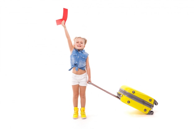 Pretty little girl in blue shirt, white shorts and sunglasses hold yellow suitcase by the handle